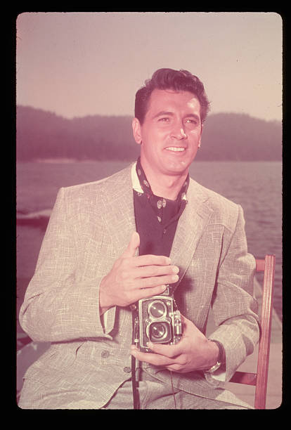 Famous actor Rock Hudson sits along the water holding a twin-lens - Old Photo